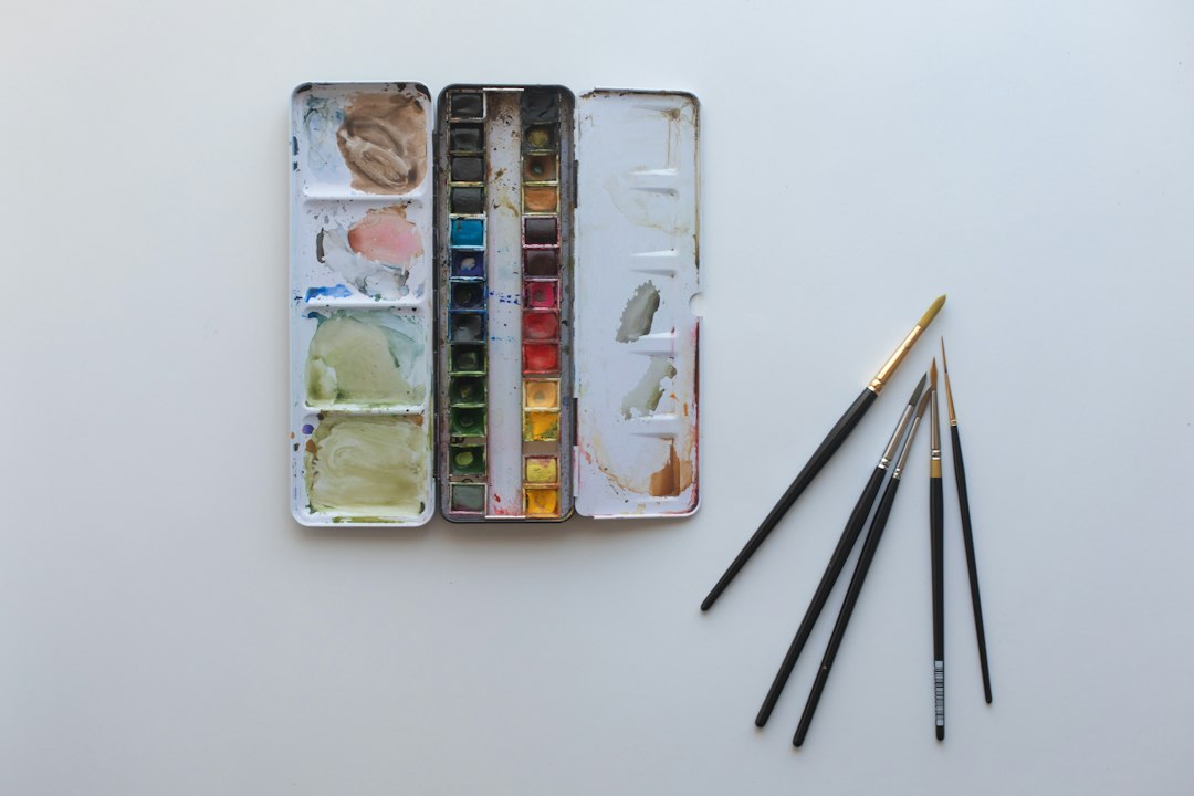 علبة ألوان مائية وفرش رسم مرتبة على سطح عمل خالٍ
